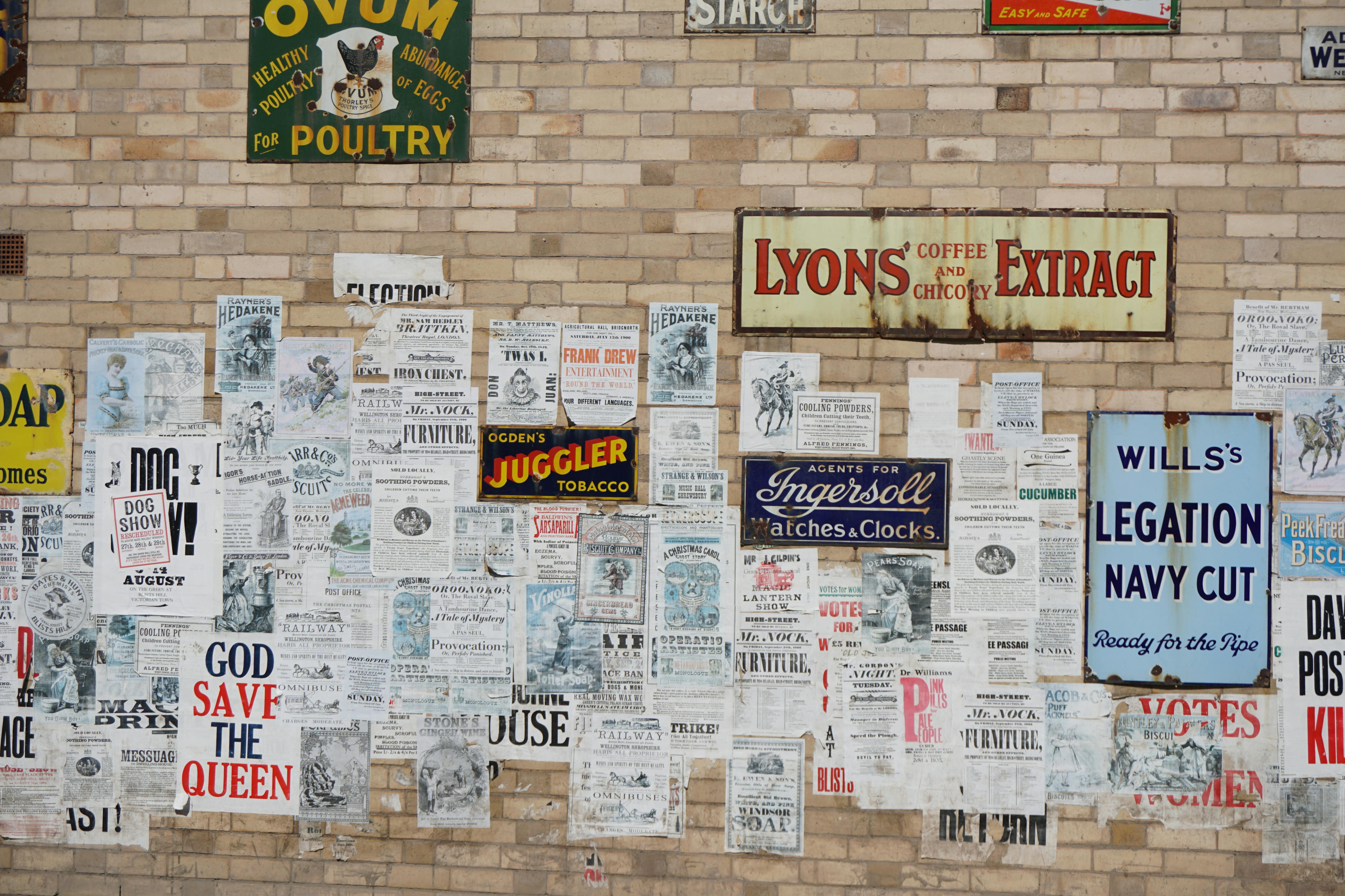 A collection of vintage posters on a brick wall, showcasing historic advertisements and text.