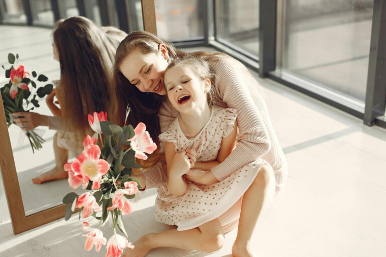 A loving mother and daughter duo laughing joyfully with a bouquet indoors.