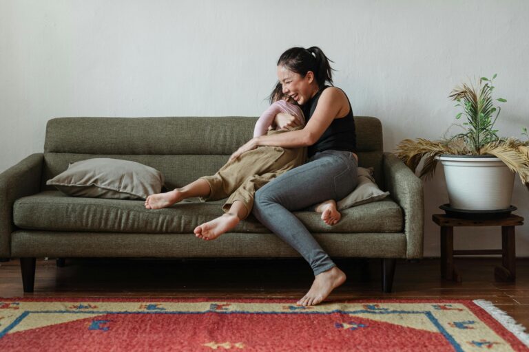 A happy mother and daughter laughing together on a cozy living room sofa.