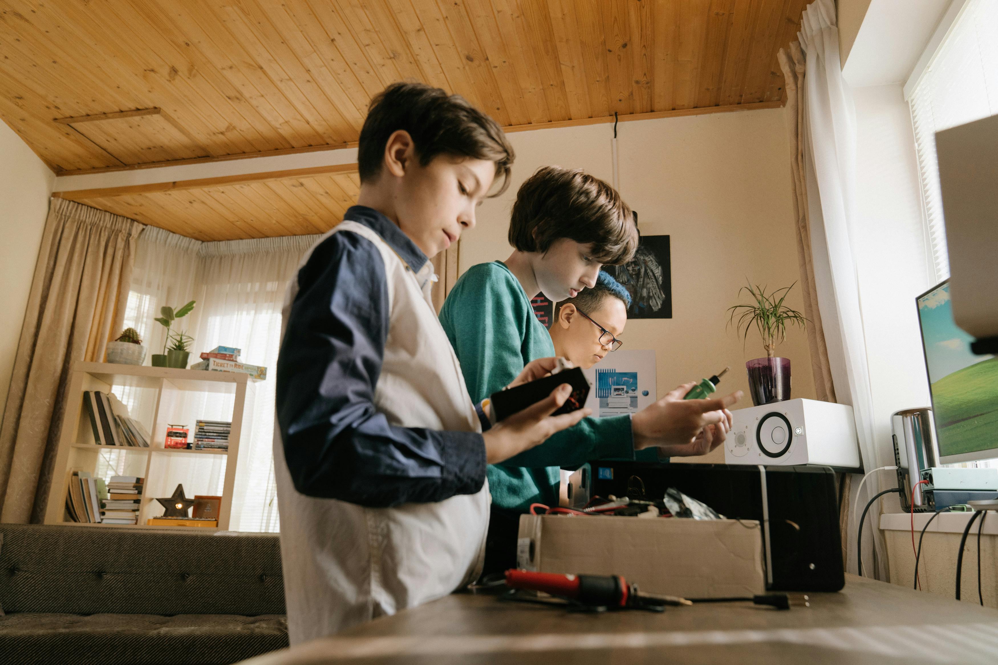 Three kids exploring tech projects indoors, focusing on electronics and creativity.