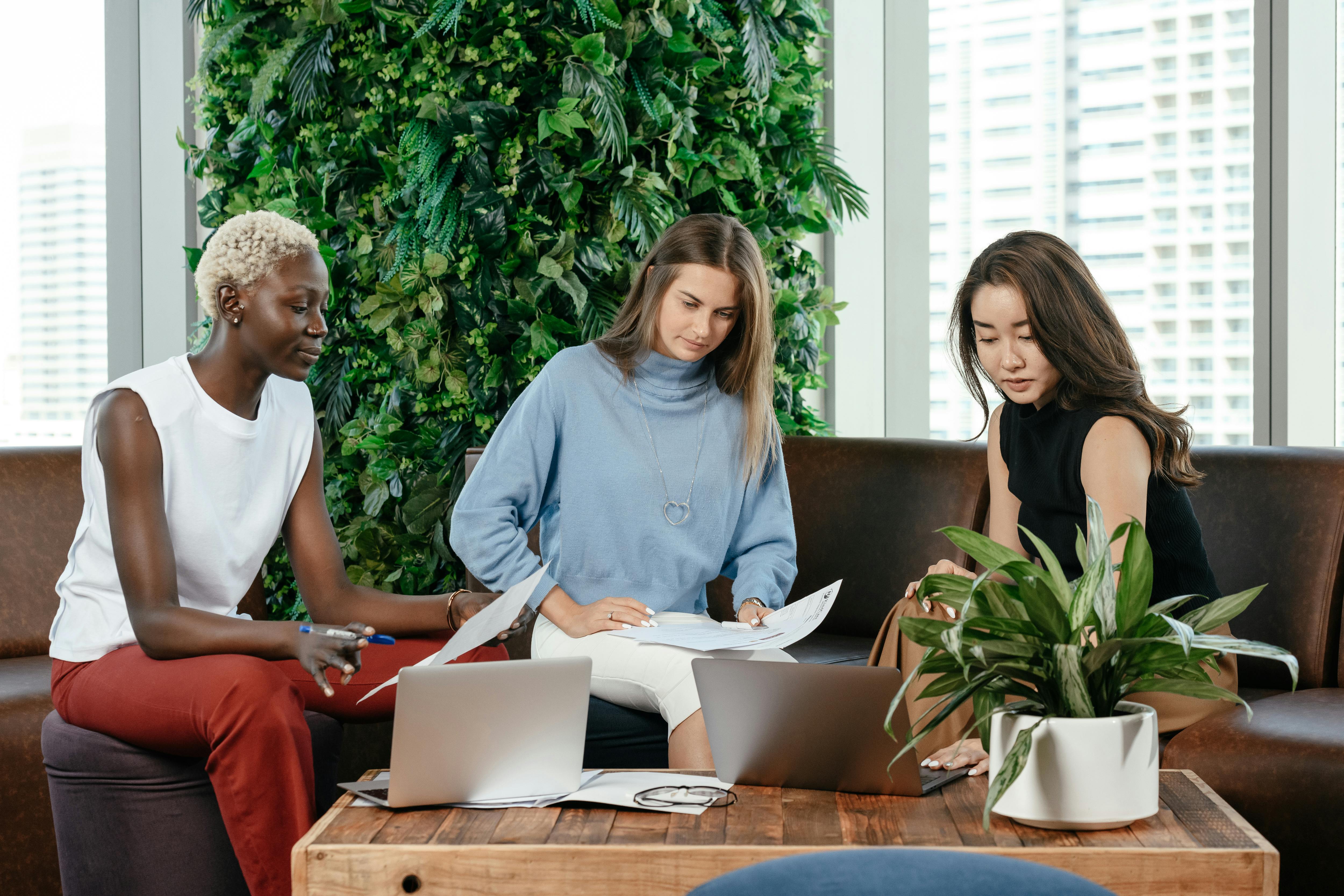 Three diverse women working together in a modern office with laptops and documents.